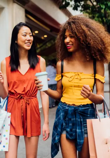 two women holding shopping bags and walking outside