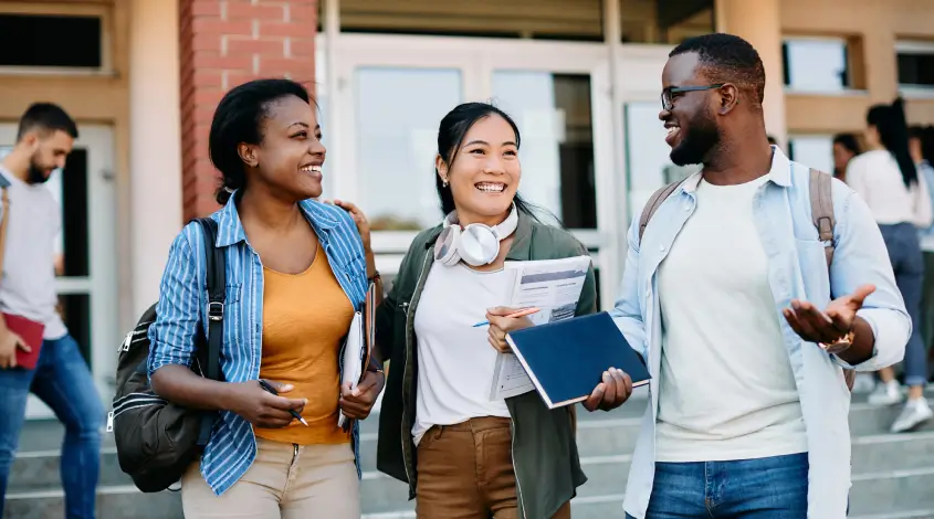 a group of three students standing outside of a college building